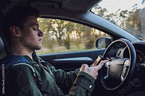 young white man driving a modern car with focusing on his smartphone