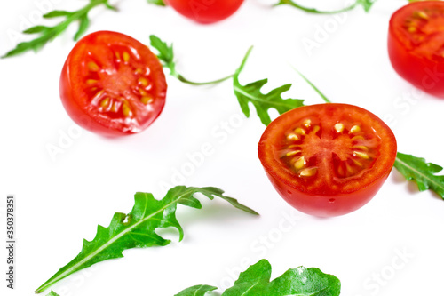 Halved red cherry tomatoes with green rucola leaves isolated on a white background.