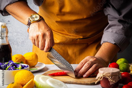 Male slicing chilli pepper on wooden cutting board by Japanese kitchen damaskus knife (Santoku) to preparation for meal in home kitchen photo