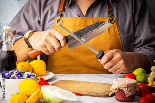 Male hand holding and sharpening Japanese kitchen damaskus knife (Santoku) to preparation for meal in home kitchen