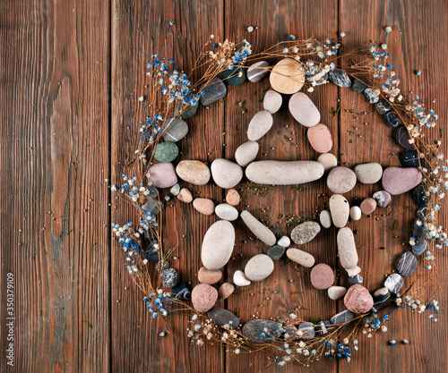 Pentagram made of stones with dry flowers of gypsophila on a wooden background. Top view. photo
