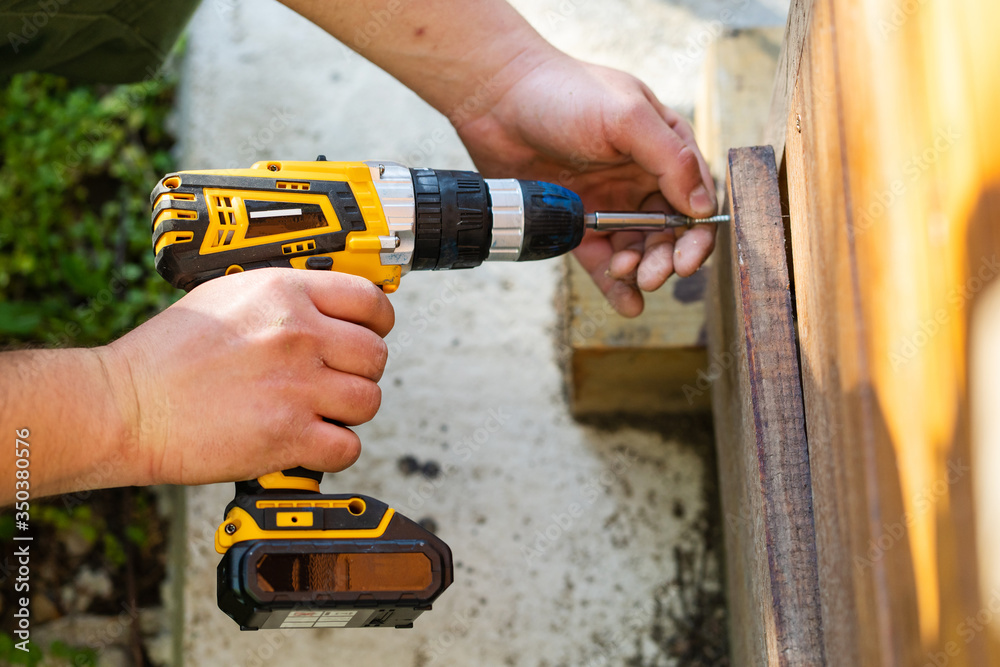 Close up on unknown man caucasian hand holding yellow electric cordless screwdriver working outdoor screwing technician on site work using hand tools concept in day high angle view