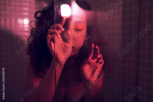 Lonely creative portrait of a woman in a shower behind a glass with powerful moody light