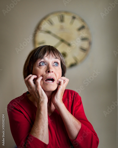 Εκτύπωση καμβά Woman curls her fingers into her cheeks, seemingly reacting in fright to time on large wall clock behind her
