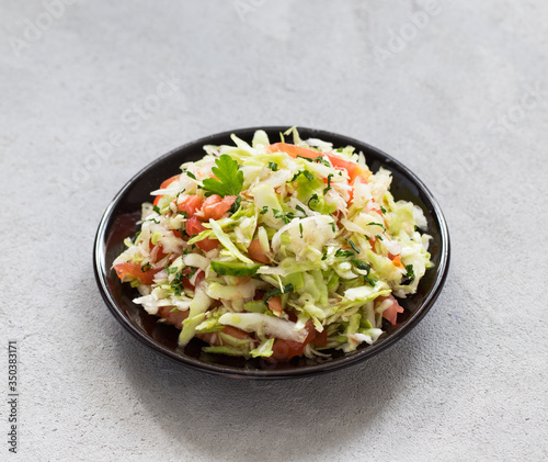 Salad of fresh vegetables cabbage and tomatoes with parsley and green onion on a plate on a light background