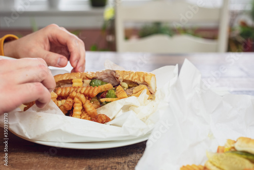 Closeup of a young man enjoying an Italian beef sandwich and fries at home