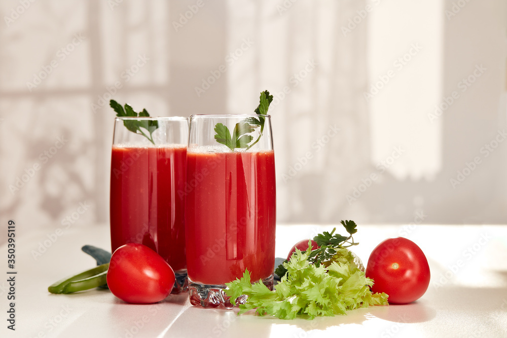 Two glasses with fresh tomato juice and ripe tomatoes on white table near window. Two glasses with fresh tomato juice and ripe tomatoes on white table near window.