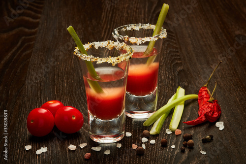 Two shot glasses with cocktail Bloody Mary on dark wooden background