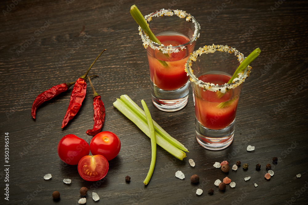 Two shot glasses with cocktail Bloody Mary on dark wooden background - obrazy, fototapety, plakaty 