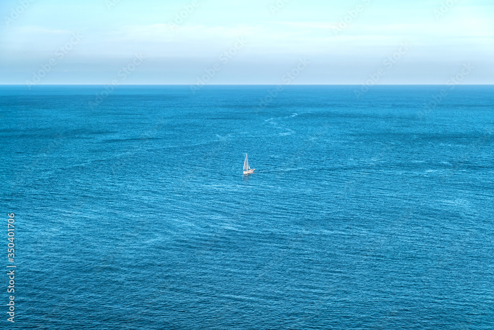 White sailboat sailing in vast aquamarine blue sea
