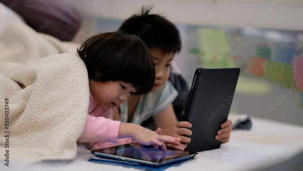 two chinese children addicted tablet, asian child watching tablet, kid use telephone together on their bed, play phone, kid addict smartphone
