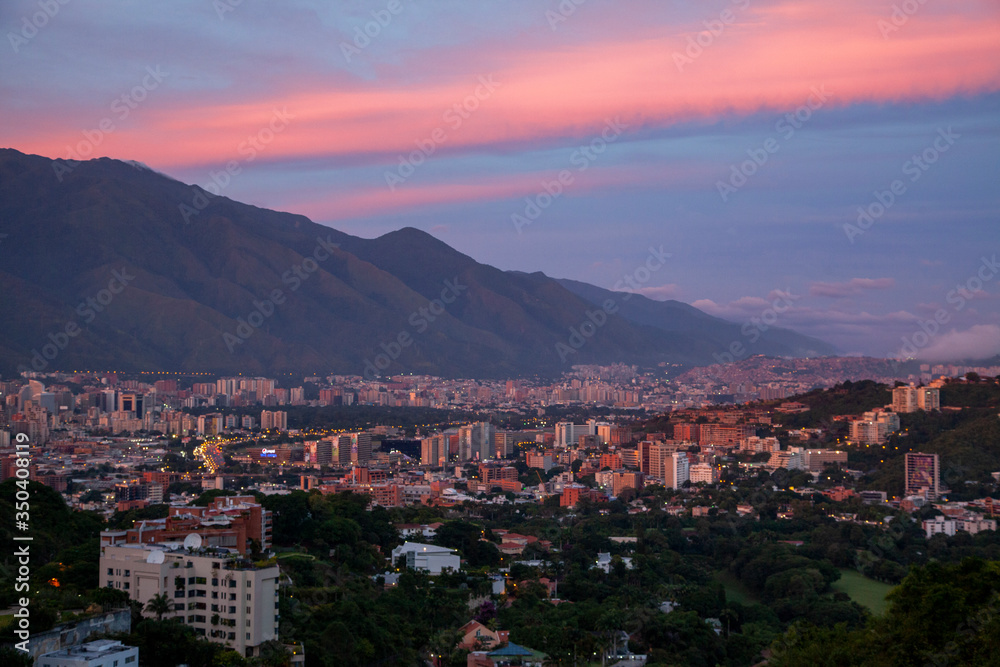 The setting sun paints the clouds above the mountains and buildings of Caracas, Venezuela.