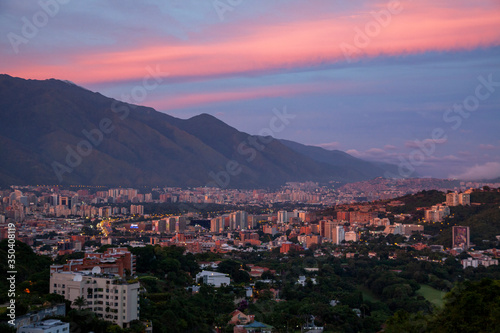The setting sun paints the clouds above the mountains and buildings of Caracas, Venezuela.