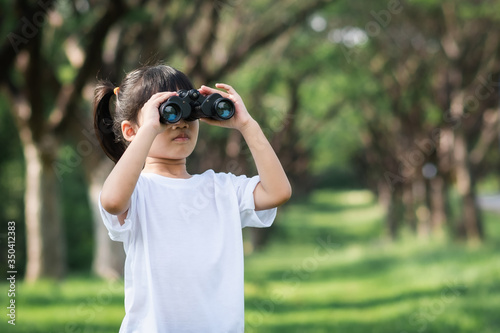 little girl use binoculars in summer garden on warm  day outdoors.