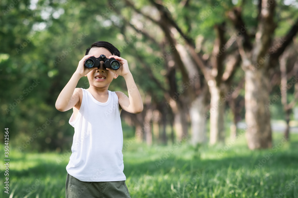 little boy use binoculars in summer garden on warm  day outdoors..