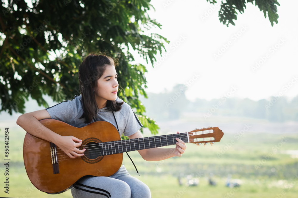 Obraz premium Beautiful young woman playing guitar at sunset, fashion lifestyle