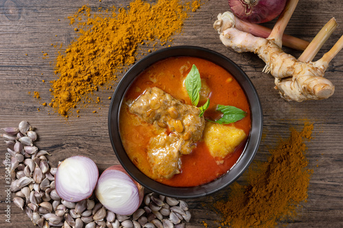 Chicken massaman curry in black bowl with herb , spices and curry powder on wooden background. Thai authentic food called massaman kai. top view. Flat lay. photo