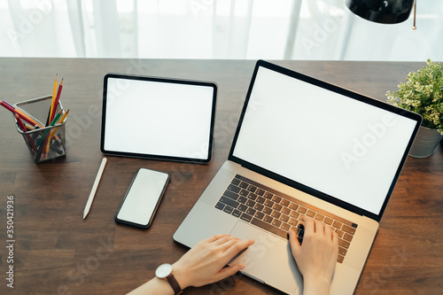 Woman using digital laptop and tablet with smartphone on the table in house. Blank screen for advertising.