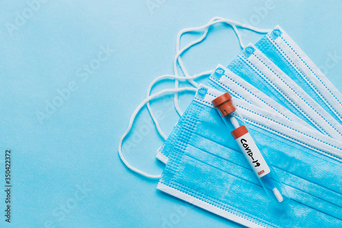 One single glass test tube containing a Corona virus test swab sitting on top of some blue surgical masks  photo