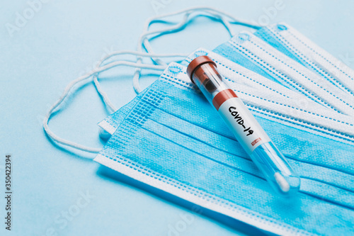 One single glass test tube containing a Corona virus test swab sitting on top of some blue surgical masks  photo