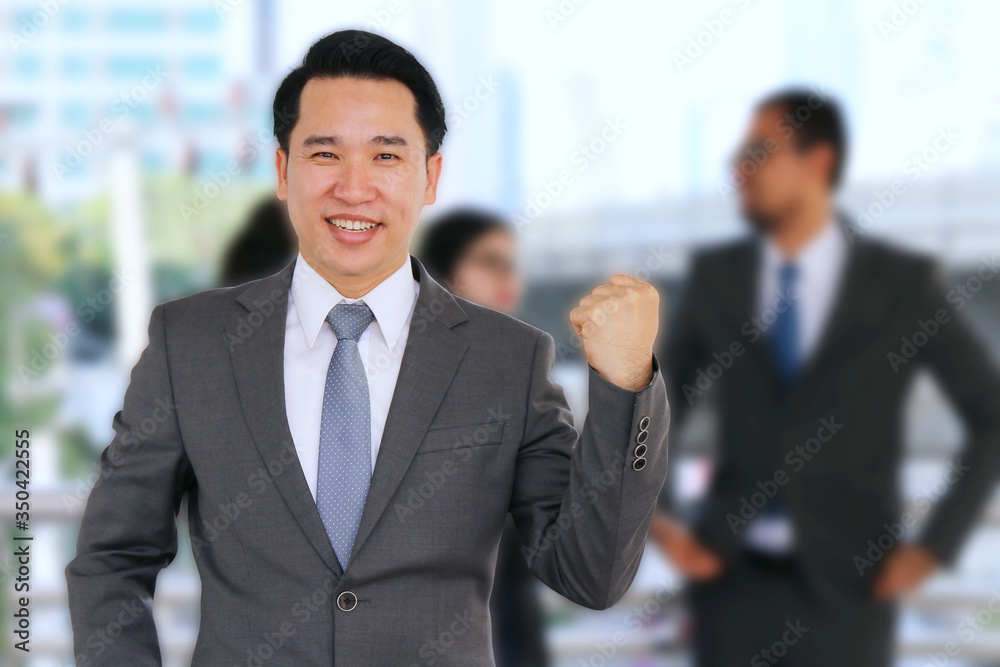 Smiling and happy businessman posing while colleagues talking to Smiling and happy businessman posing while colleagues talking to