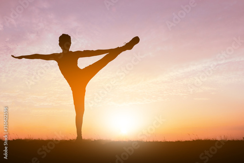 Silhouette of gorgeous young woman practicing yoga in sunset sky background.