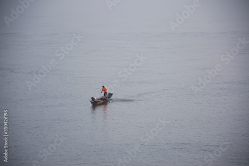 Thai and laos people riding long tail boat for catch fishing and reflection light surface water of Mekhong River and lighting of Sun in morning time at Mukdahan, Thailand