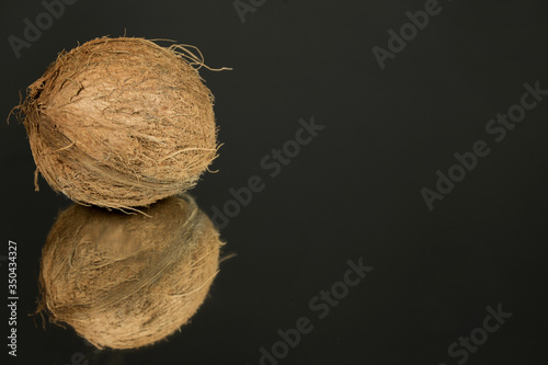 Large shaggy coconut isolated on a black mirror surface with reflection