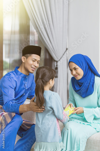 Muslim girl receiving green envelope from parents during Eid al-Fitr
