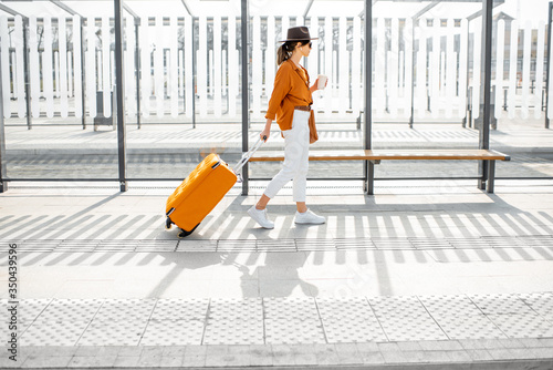 Young female traveler with a suitcase at the transport stop