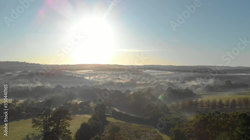 Aerial shot moving forward into a beautiful sunrise with early morning fog over the green lush landscape. photo