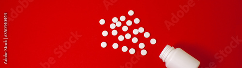 concept of exploding pills from a bottle. White round pills and jar of on the table. Medical drugs on a red background. White tablets isolated.