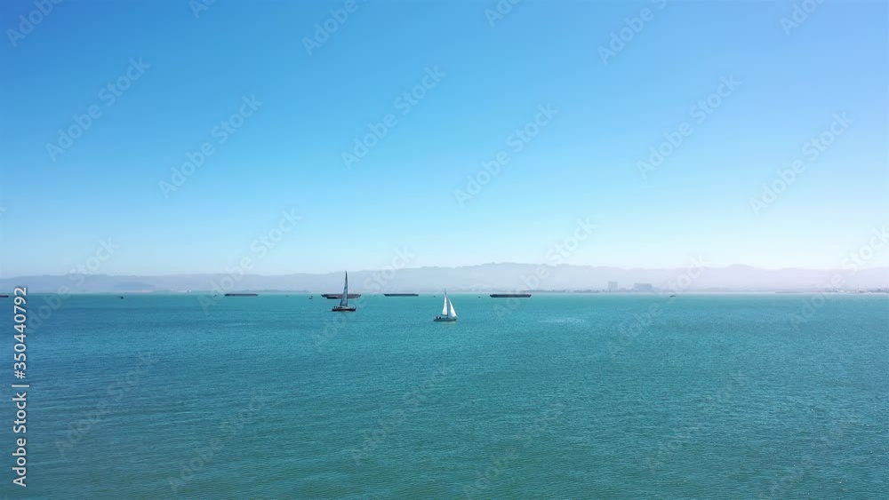 Two sailboats sail in blue ocean bay water on beautiful sunny day, aerial Two sailboats sail in blue ocean bay water on beautiful sunny day, aerial