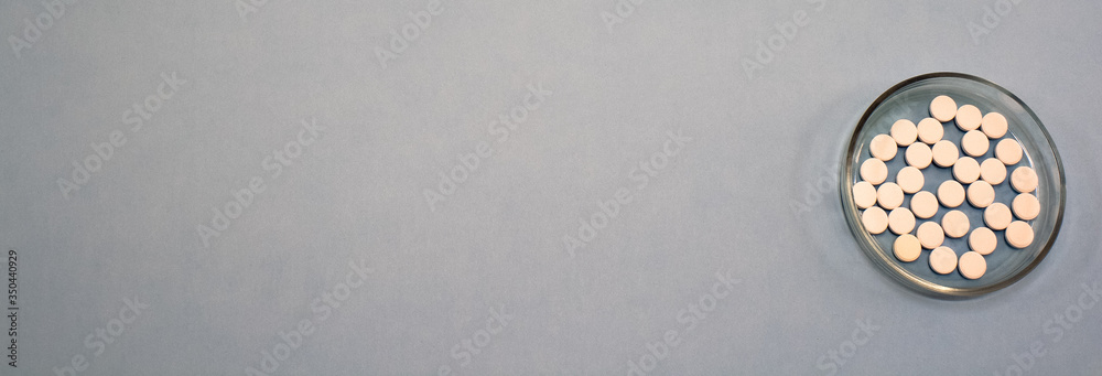 White pills, drugs in the transparent bowl on grey background. Prevention of coronavirus. Web banner on site with empty space for text on the left side. Isolated. Medical preparations close up White pills, drugs in the transparent bowl on grey background. Prevention of coronavirus. Web banner on site with empty space for text on the left side. Isolated. Medical preparations close up