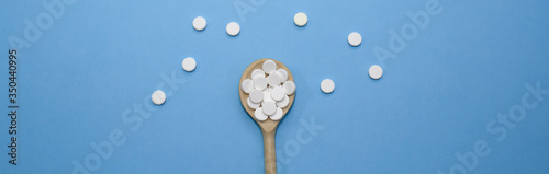 White pills are scattered on a blue background. White drugs on a wooden spoon. Treatment of patients for the virus. Strengthening the immune system. Web banner.