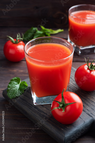 Tomato juice in glass glasses and fresh ripe tomatoes on a branch. Dark wooden background with copy space.