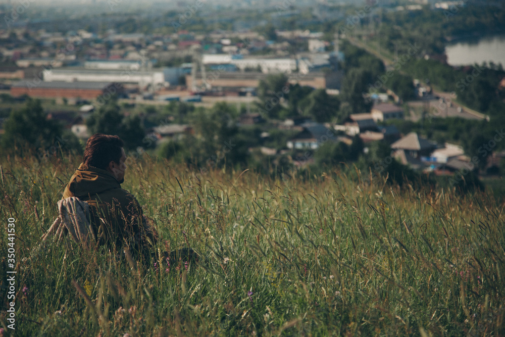 Obraz premium Man against the background of wild nature. Russian mountains, plains, fields. the traveler sits in the tall grass and looks into the distance