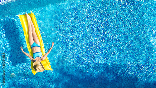 Girl relaxing in swimming pool, child swims on inflatable mattress and has fun in water on family vacation, tropical holiday resort, aerial drone view from above 