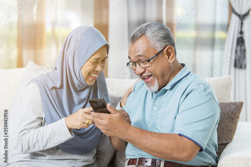 Senior couple laughing together while holding the smartphone photo