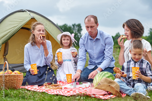 Happy family having picnic in meadow on a sunny day. Family Enjoying Camping Holiday In Countryside