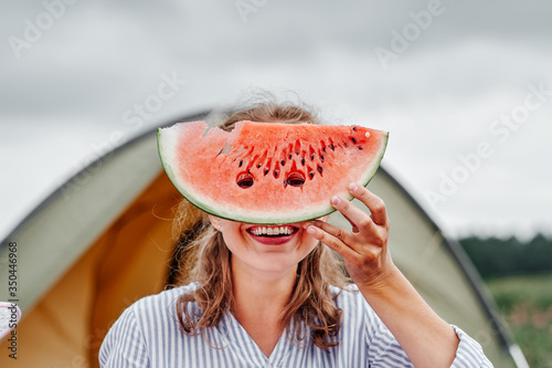 Funny woman eating watermelon on a picnic. Girl closed her eyes with a watermelon, looking into the holes