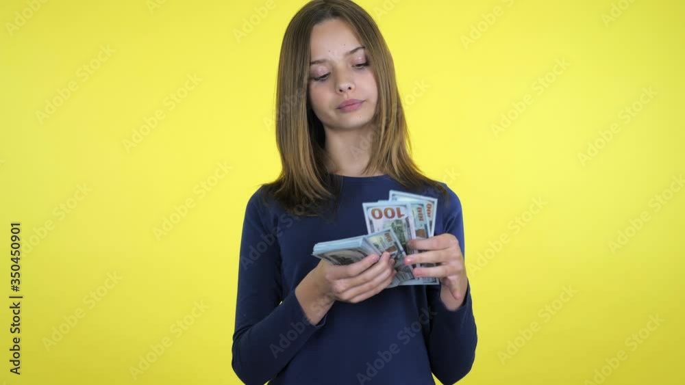 Rich teenager girl in a blue sweater counts money and thinks that she will buy it on yellow background with copy space. Place for text or product. 4K slowmotion footage Rich teenager girl in a blue sweater counts money and thinks that she will buy it on yellow background with copy space. Place for text or product. 4K slowmotion footage