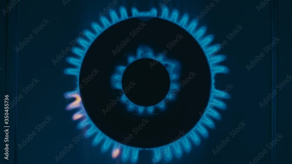 The gas stove burner ignites with a blue flame in the dark. A powerful burner WOK with two rows of flame (two rings of fire) looks beautiful and heats food faster. Top view The gas stove burner ignites with a blue flame in the dark. A powerful burner WOK with two rows of flame (two rings of fire) looks beautiful and heats food faster. Top view