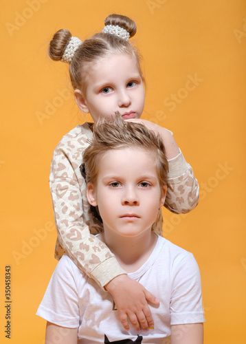 boy hugs a girl,  brother and sister on yellow background photo