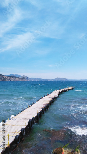 Photos from the phone. Seascape with a wooden pier for boats. Picturesque sea and mountains. Blue sky with clouds. Copy space.
