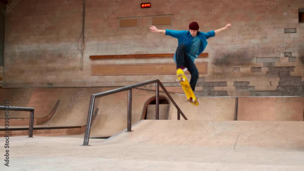 Young Caucasian skater wearing casual clothes and sneakers training skateboard flip on railing in modern skating arena