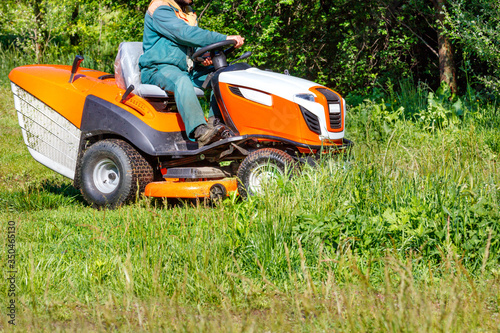 A gardener mows tall green grass with a tractor lawn mower.