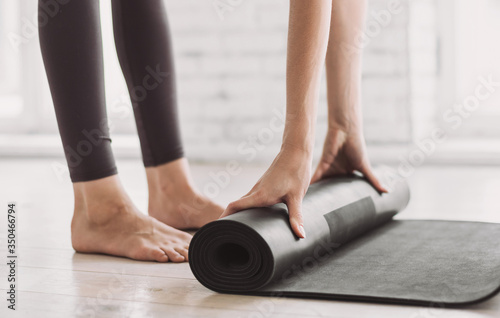 Female hands rolling up exercise mat and preparing doing yoga. Young woman meditating at home. Girl practicing yoga in class. Relaxation, body care, healthy lifestyle, exercising, training concept