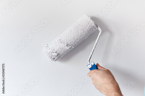 Fototapeta Naklejka Na Ścianę i Meble -  Left hand man's hand painting the wall with paint roller. Painting apartment, renovating with white color paint