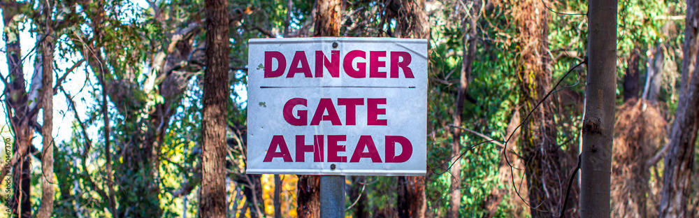 A striking red danger sign posted in the Australian bush in autumn, featuring yellow and green fall foliage.